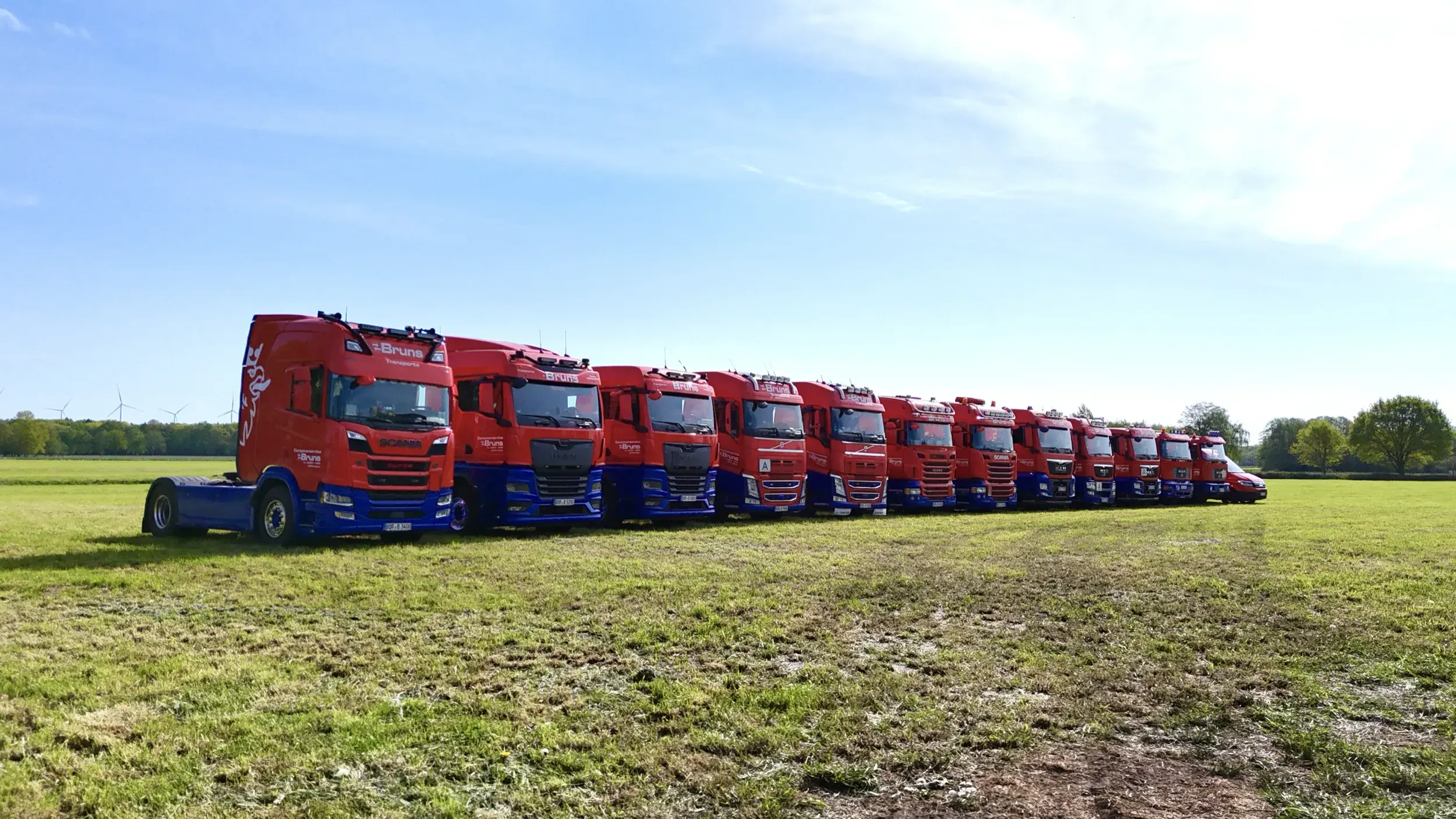Luftaufnahme: Sattelzugmaschinen von Bruns Transporte in einer Reihe auf einer Wiese
