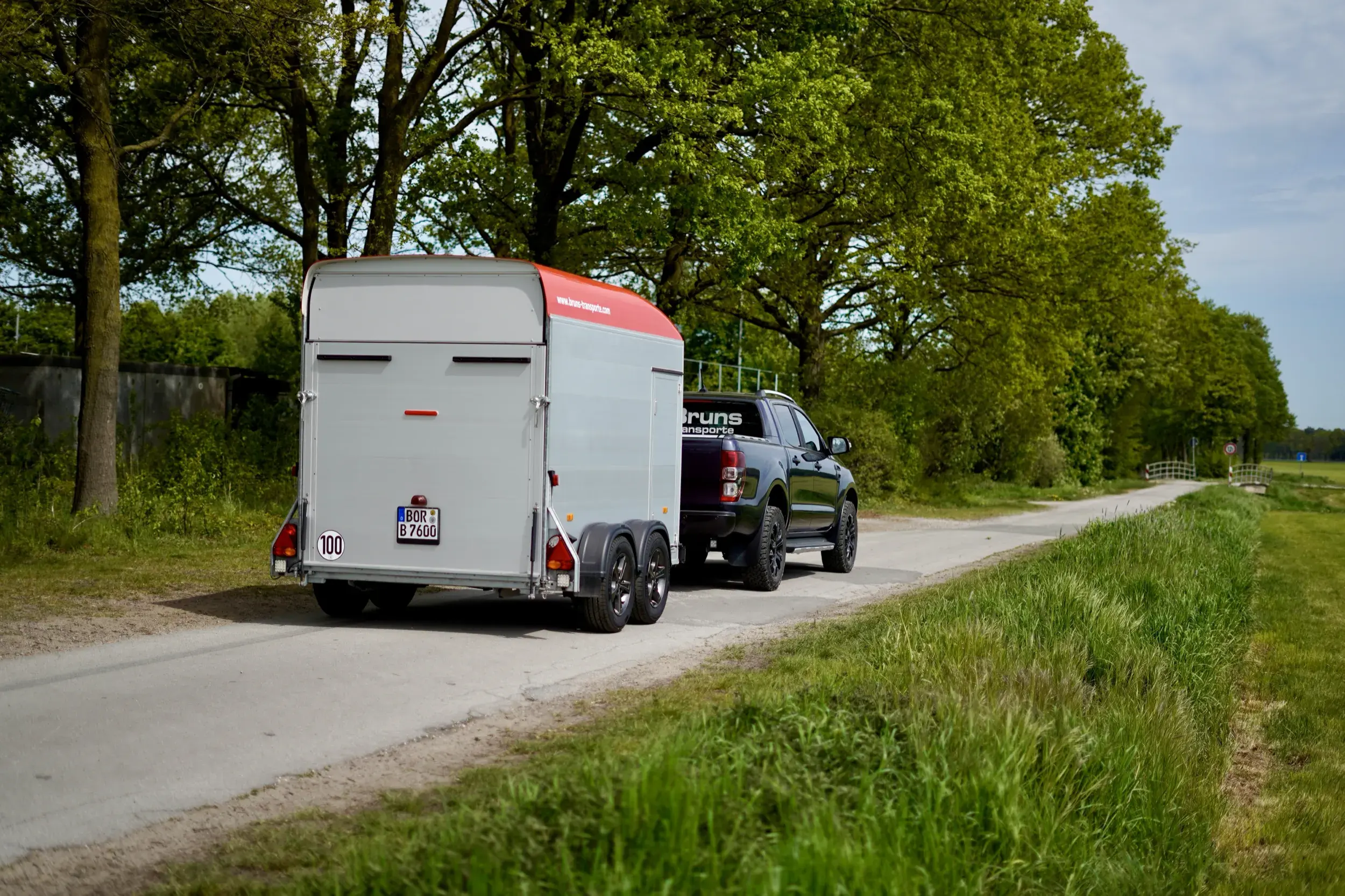 Silberner Kofferanhänger hinter einem Pick-up auf einem Feldweg