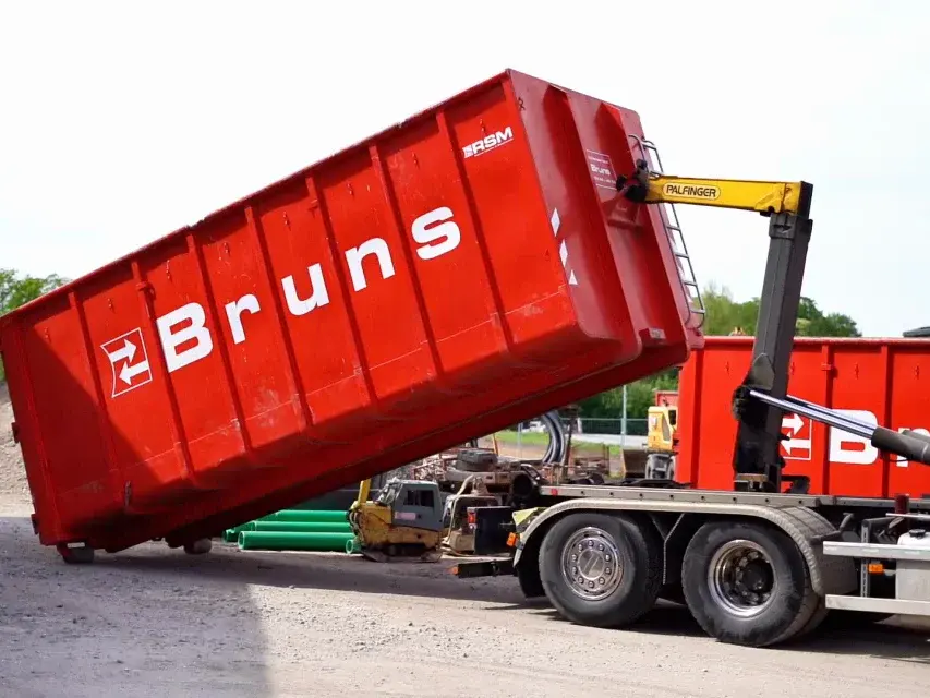 Abrollkipper von Bruns Transporte setzt einen roten Abrollcontainer ab
