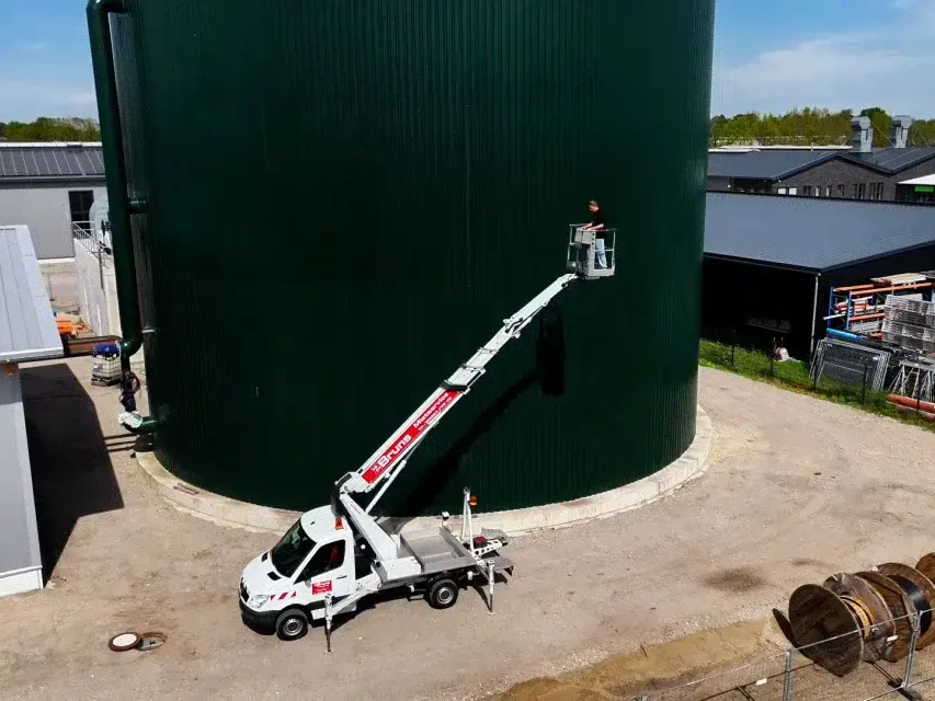 Hubarbeitsbühne TBR200 auf weißem Transporter mit ausgefahrenem Korb vor einem grünen Silo